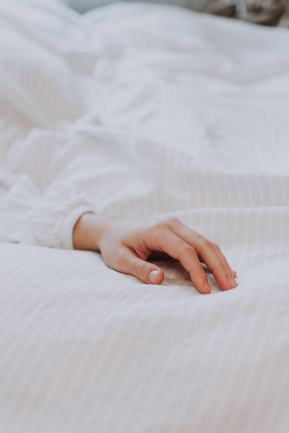 A lonely female hand on a soft bed linen, the concept of fatigue and loneliness - Foto, immagini