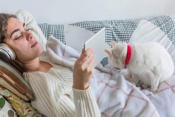 A young Caucasian girl with headphones enjoying multimedia content on a tablet while lying on a sofa - Фото, изображение