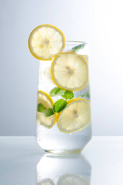 A glass of invigorating water with lemon slices and mint leaves on a reflecting surface - Φωτογραφία, εικόνα