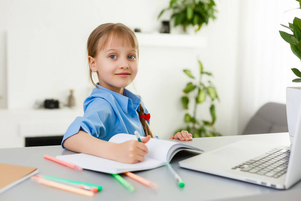 Schattig klein meisje zit aan tafel met haar laptop en studeren online - Foto, afbeelding