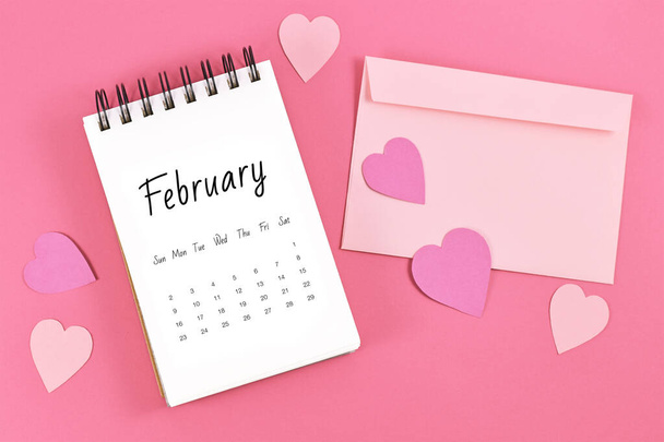 Flat lay with February calendar sheet with Valentine's Day on the 14th surrounded by hearts and love letter on pink background - Foto, Imagem