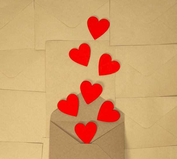 バレンタインデークラフトエンベロープ茶色の無地の紙の背景に赤いハート、ロマンチックな愛のデザイントップビュー、コピースペース - 写真・画像