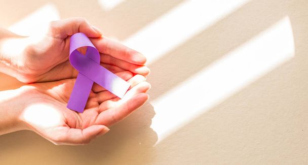 A high angle shot of a female hand holding a purple ribbon on brown background - Foto, immagini