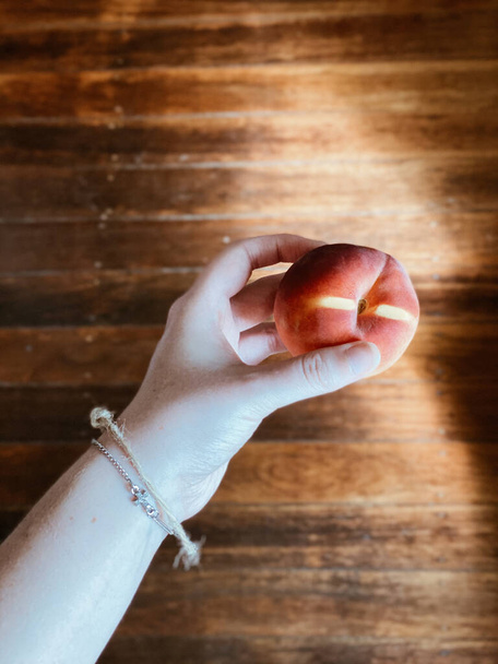 A top view of a hand holding a peach in sunlight on  a wooden background - still life - 写真・画像