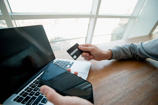 Male hands hold smartphone and credit card with laptop on background. Dont enter your credit card details on suspicious sites. Man using card to make an online purchase. Financial literacy concept. - Photo, Image