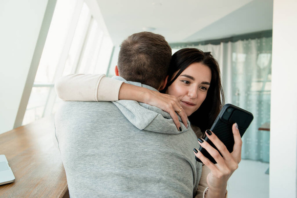 Woman texting other men when embracing her boyfriend. Lies will always pop up concept. Man trusts his wife but she deceives him. Cheating concept. Woman looking in her smartphone while hugging man. - Foto, immagini