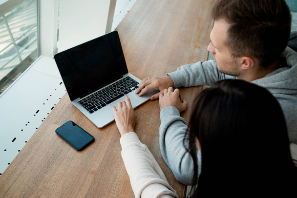 Чоловік і жінка працюють на ноутбуці разом. Колеги сидять у кав'ярні, щоб працювати над спільним проектом. Концепція коворкінгу. Кав'ярня на фоні. Сучасний сірий ноутбук
. - Фото, зображення