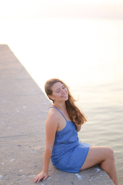 jong Kaukasisch meisje zitten op pier en het dragen van sundress - Foto, afbeelding