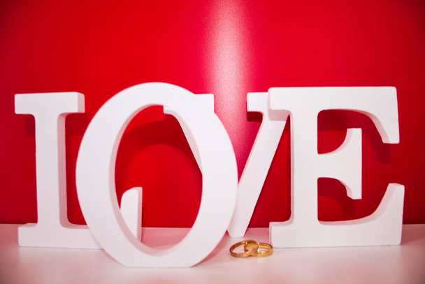 anelli nuziali in oro su sfondo rosso e bianco per San Valentino e la parola amore - Foto, immagini