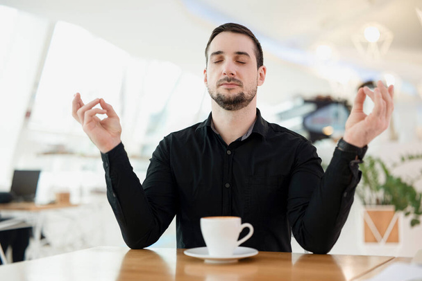 Mantenha a calma e beba uma xícara de bom café expresso. O homem está meditando porque, devido à grande quantidade de cafeína, ele teve um ataque de pânico. Café no fundo. Homem elegante. - Foto, Imagem