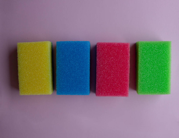 quattro spugna di gomma piuma colorata per pulire e lavare i piatti su sfondo rosa.  - Foto, immagini
