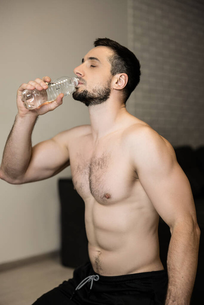 Topless homem atraente água potável após o treino duro em casa. Tempo de descanso. Homem musculoso esportivo bebendo água após o exercício. Treino de musculação. Conceito de hidratação e fitness. - Foto, Imagem