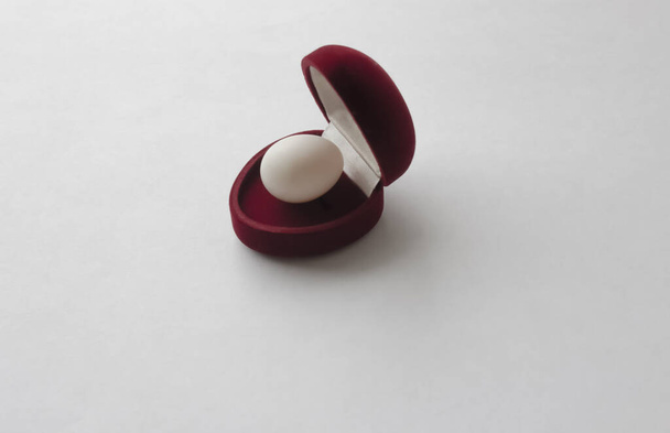 Scatola di velluto rosso per una fede nuziale con un uovo dentro su uno sfondo bianco. Concetto d'amore. San Valentino. - Foto, immagini