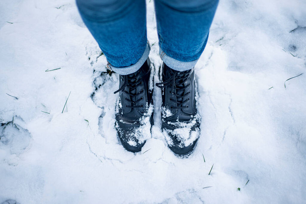 черные сапоги со шнурками в снегу, морозная погода, снежные ботинки, зимняя атмосфера - Фото, изображение
