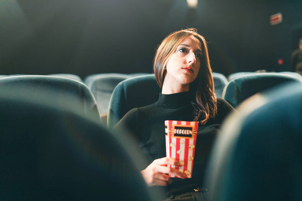 Genç bir kadın patlamış mısır yiyor ve sinemada film seyrediyor. - Fotoğraf, Görsel