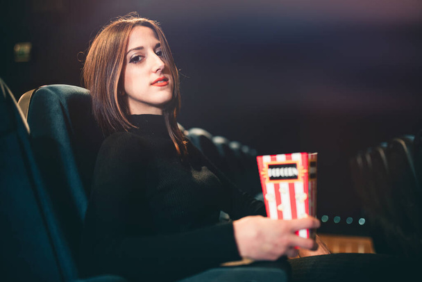 young woman eating popcorn and watching a movie at the cinema theater - Foto, Imagem