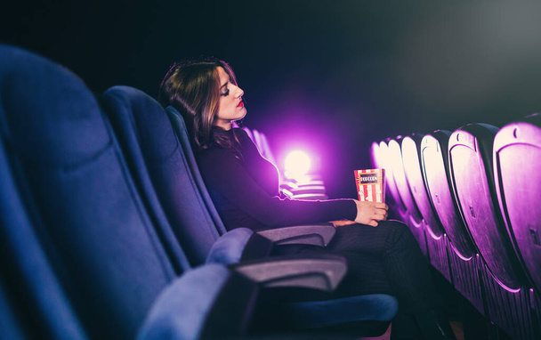 young woman holding popcorn and sleeping at the cinema theater - Foto, Imagem