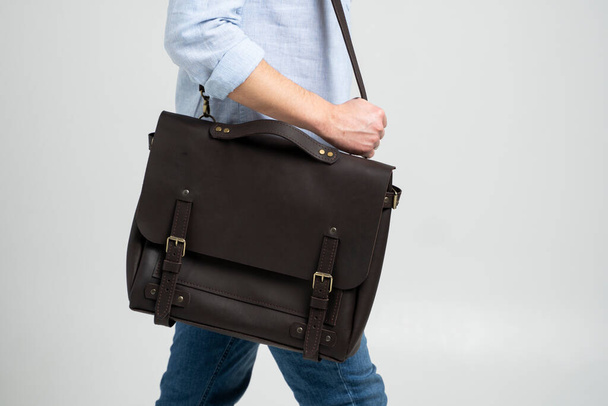 Brown mens shoulder leather bag for a documents and laptop on the shoulders of a man in a blue shirt and jeans with a white background. Satchel, mens leather handmade briefcase. - Foto, Bild
