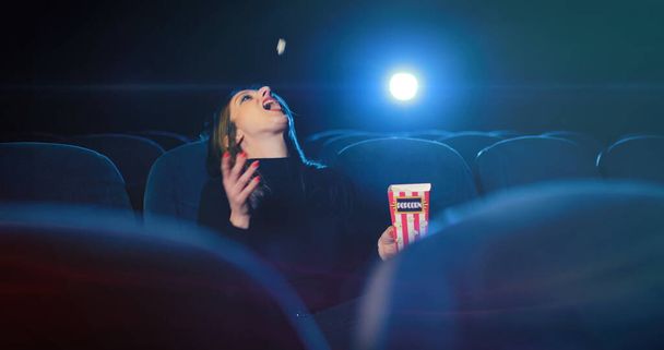 jonge vrouw vangen popcorn door haar mond in de bioscoop - Foto, afbeelding