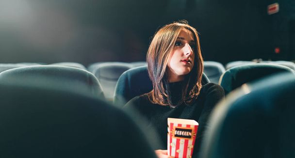 молода жінка їсть попкорн і дивиться фільм в кінотеатрі
 - Фото, зображення