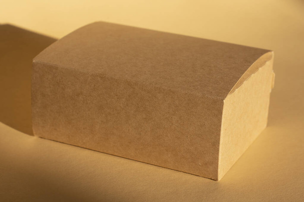 brązowe kartonowe pudełko na beżowym tle i jego cieniu. Pakowanie - Zdjęcie, obraz
