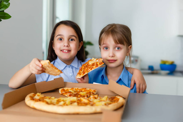 Two happy little child girl friends eating pizza slices. - Foto, imagen