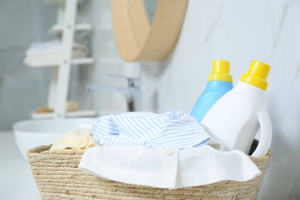 Bottles of detergent and children's clothes in wicker basket indoors, closeup - Fotó, kép