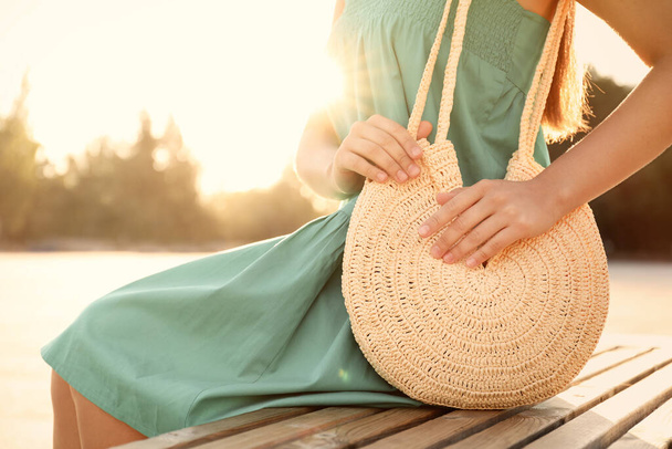 Young woman with stylish straw bag on bench outdoors, closeup - Foto, Imagen
