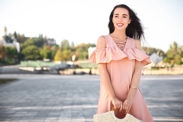Beautiful young woman in stylish pink dress with handbag on city street - Foto, afbeelding