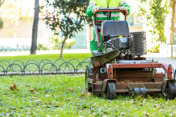 неузнаваемый муниципальный оператор косит траву автоматической косилкой в парке - Фото, изображение