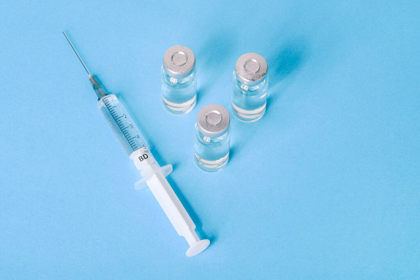 COVID-19 szczepionka na niebieskim tle. Fiolka ze szczepionką do leczenia koronawirusów. Koncepcja leczenia wirusami korony, zastrzyk. Badania szczepionek podczas pandemii - Zdjęcie, obraz