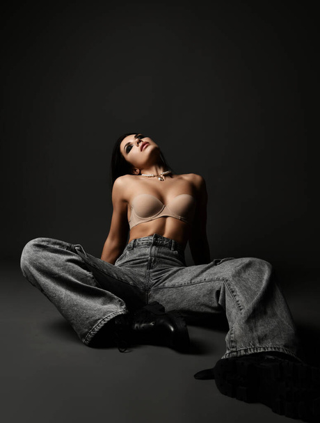 Young pretty sexy brunette woman model in denim jeans and bra sitting on floor with eyes closed showing perfect body - Фото, изображение