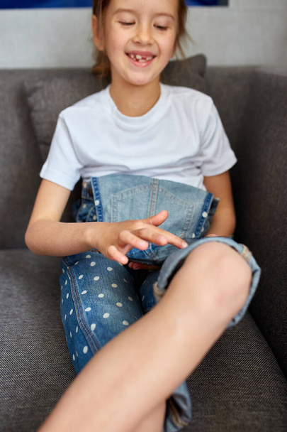 Linda niña usando una tableta digital, sentada en el sofá, jugando y sonriendo, o un niño en casa viendo dibujos animados en la computadora portátil. Niño moderno y tecnología de la educación
. - Foto, imagen