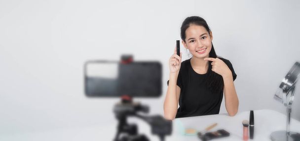 美人ブロガー。アジアの10代の女性がカメラの前に座って、美容ブロガーのインフルエンサーやyoutuberとしてライブ放送自宅で構成する方法についてのレビューやアドバイスをします。スタジオは白地を撃った. - 写真・画像