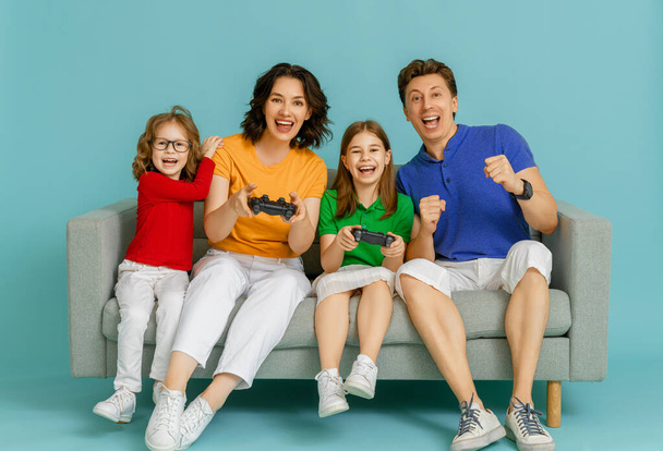 Happy family together. Mother, father and their children girls playing video games. People having fun on bright blue background. - Фото, изображение