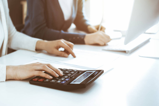 Accountant checking financial statement or counting by calculator income for tax form, hands close-up. Business woman sitting and working with colleague at the desk in office. Audit concept - 写真・画像