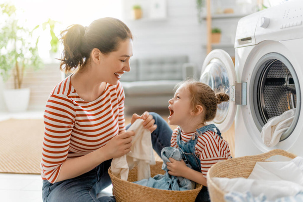 Beautiful young woman and child girl little helper are having fun and smiling while doing laundry at home. - Zdjęcie, obraz