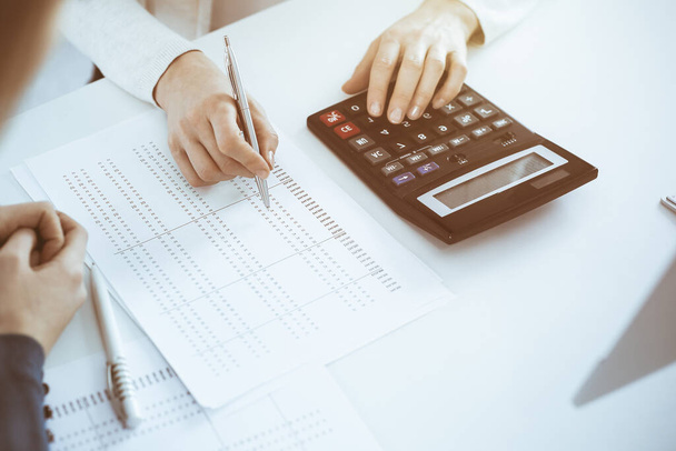 Accountant checking financial statement or counting by calculator income for tax form, hands close-up. Business woman sitting and working with colleague at the desk in office. Audit concept - Valokuva, kuva