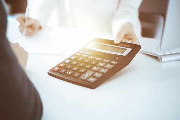 Accountant checking financial statement or counting by calculator income for tax form, hands close-up. Business woman sitting and working with colleague at the desk in office. Audit concept - Photo, image