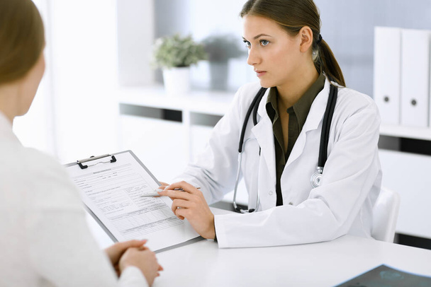 Woman-doctor and patient sitting and talking at hospital office. Green color blouse suits to therapist. Medicine and healthcare concept - Photo, image
