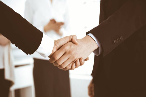 Businessman and woman shaking hands with colleagues at the background. Handshake at meeting in office. Concept of success in business - Photo, Image