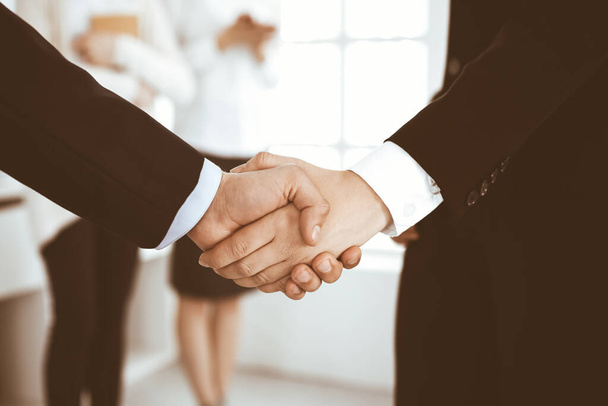 Businessman and woman shaking hands with colleagues at the background. Handshake at meeting in office. Concept of success in business - Foto, immagini