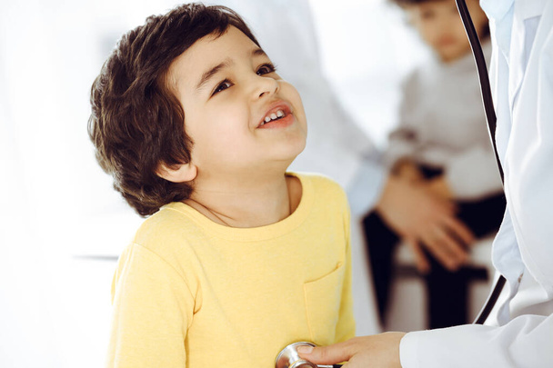 Woman-doctor examining a child patient by stethoscope. Cute arab boy at physician appointment. Medicine help concept - Foto, Bild