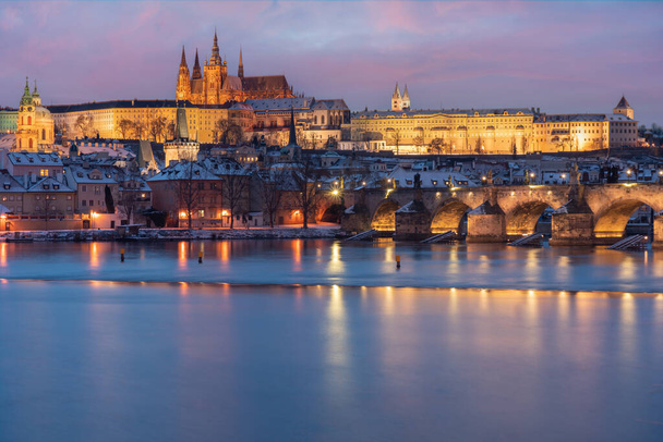 Charles Bridge on the Vltava River and Prague Castle and the Church of St. Vitus in winter and snow on the roofs in the center of Prague in the early evening - Photo, Image