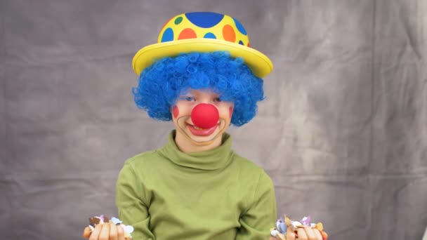 μικρό αγόρι με περούκα και μύτη κλόουν διασκεδάζει με κομφετί και σερπαντίνες γιορτάζοντας καρναβάλι - Πλάνα, βίντεο