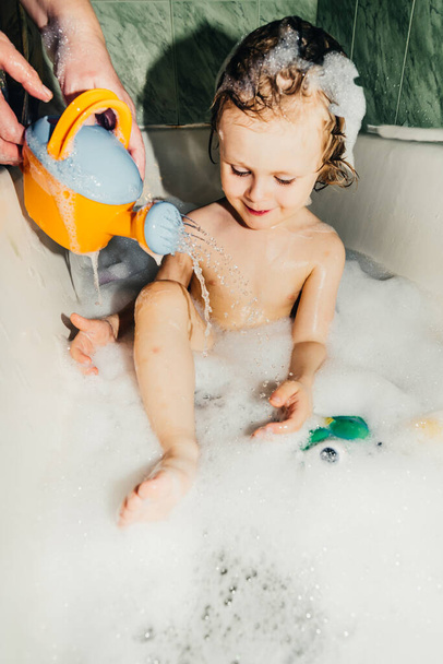 όμορφο παιδί νήπιο γιος πλένει στο μπάνιο παίζει διασκεδάζει με σαπουνόφουσκες, αφρό - Φωτογραφία, εικόνα