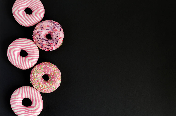 Donuts con glaseado rosa se encuentran en el fondo negro con espacio de copia y la puesta plana - Foto, imagen