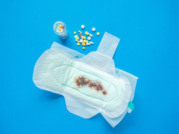 Serviette hygiénique d'une femme qui est placée avec un médicament qui se propage sur un fond bleu. - Photo, image
