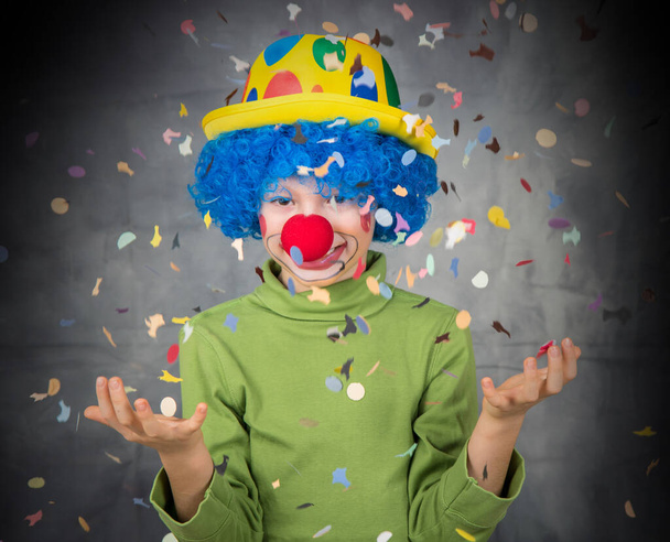 criança vestida como um palhaço com peruca e nariz falso se diverte brincando com confetes coloridos comemorando o carnaval - Foto, Imagem