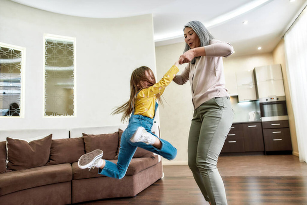 Being a grandmother is fun. Happy grandmother playing with her adorable little granddaughter, lifting her up in the air while having fun together in a living room at home - Foto, immagini